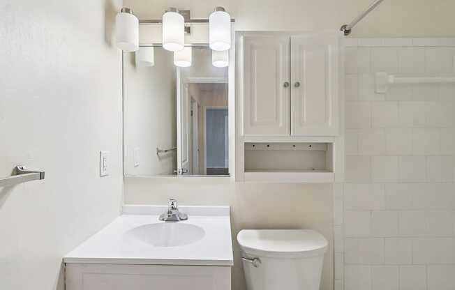 A white bathroom with a sink, toilet and cabinet.