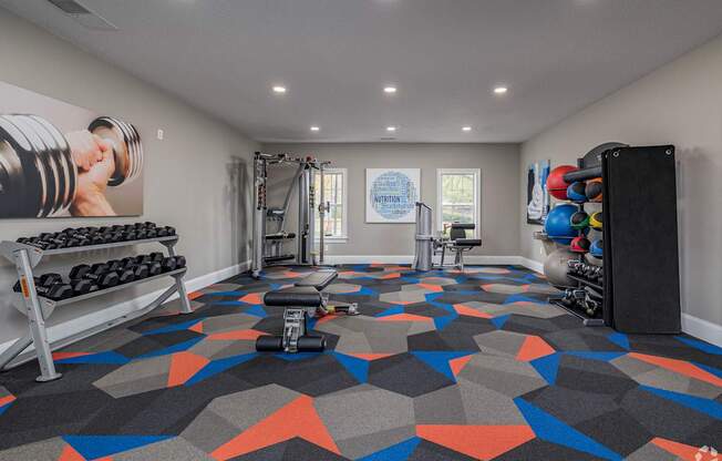 A gym with a variety of equipment including dumbbells, weight plates, and a bench press.