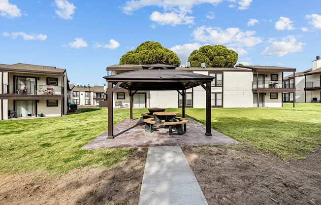 A gazebo sits in the middle of a grassy area with apartment buildings in the background.