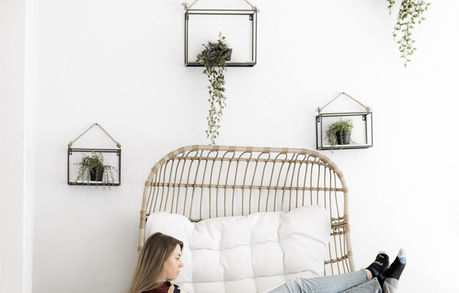 Young woman lounging in oversized chair in front of wall with hanging plants