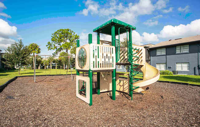 A playground with a green and white slide and a brown surface.