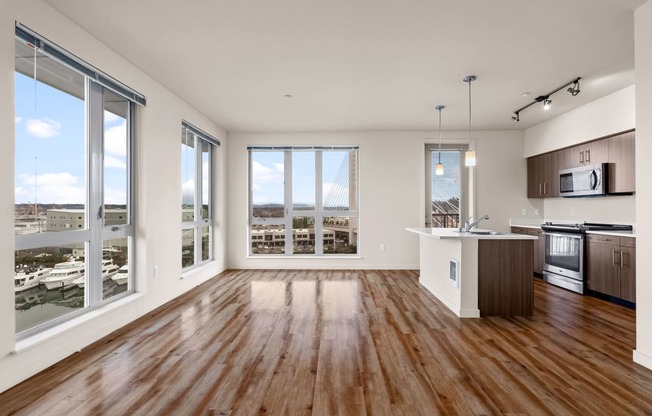 an empty living room with a kitchen and a large window