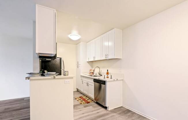 Kitchen with stainless steel dishwasher, 2 door refrigerator, double kitchen sink, wood style floors, white cabinets, light quartz counter tops, dining area on the right