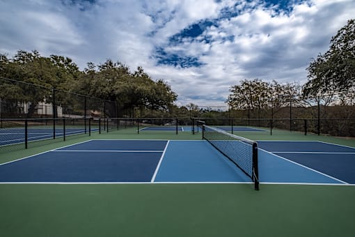 A tennis court surrounded by trees and a cloudy sky.