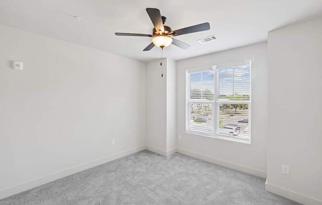 A room with a ceiling fan and a window with blinds.