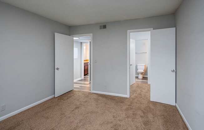 a bedroom with two doors and a bathroom in the background