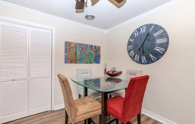 a dining room with a glass table and chairs and a large clock on the wall
