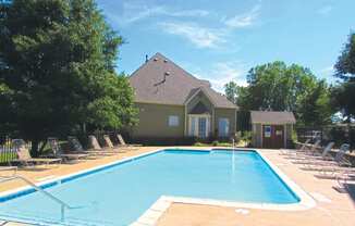 a swimming pool with chaise lounge chairs and a house in the background at GABLE HILLS Apartments, TULSA, OK
