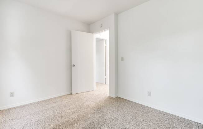 a bedroom with white walls and carpet and a door to a closet