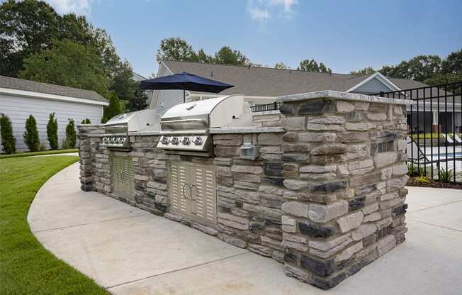 a stone outdoor kitchen with a grill on the side of a driveway