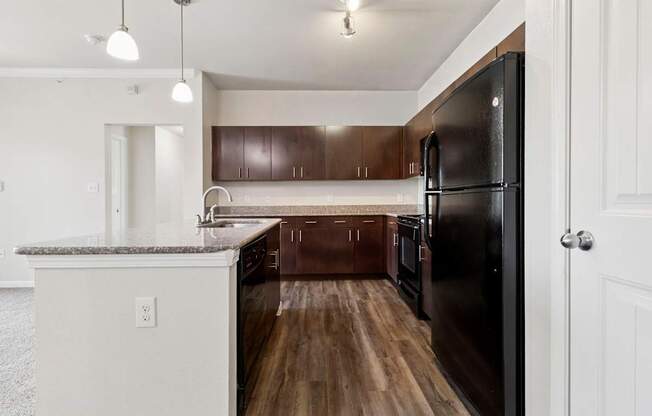 A kitchen with a black refrigerator and brown cabinets.