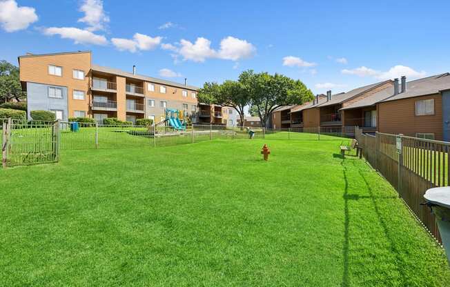 A large grassy area in front of apartment buildings with a playground and a fire hydrant.
