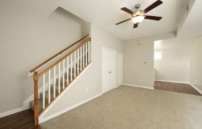 an empty living room with a ceiling fan and a staircase