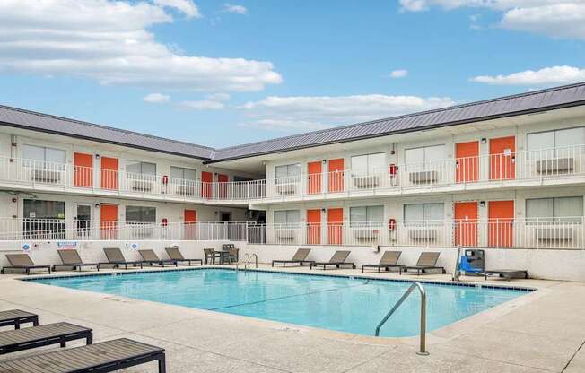 A swimming pool is surrounded by lounge chairs in front of apartment buildings.