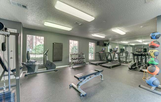 A gym with a variety of equipment including a bench press, a treadmill, and a rowing machine at Copper Hill Apartments, Texas, 76021