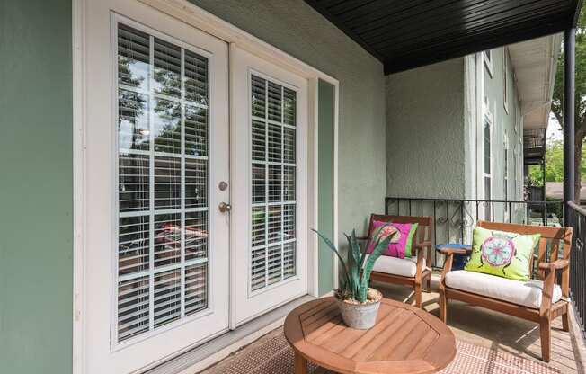 A patio with a table, two chairs and a potted plant.