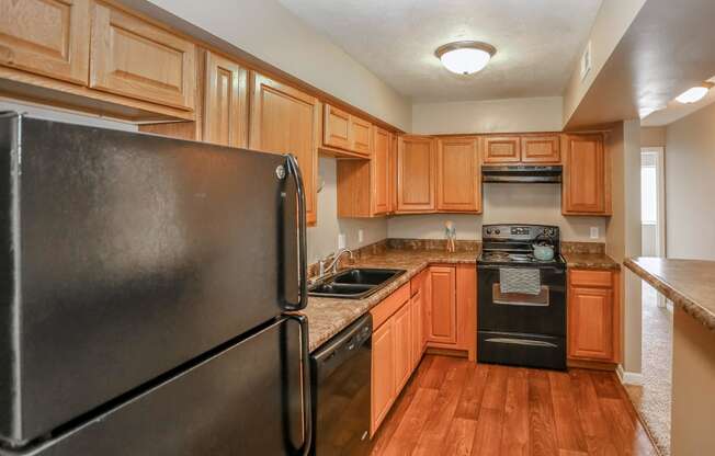 a kitchen with wooden cabinets and appliances and a black refrigerator. Omaha, NE Evergreen Terrace Apartments
