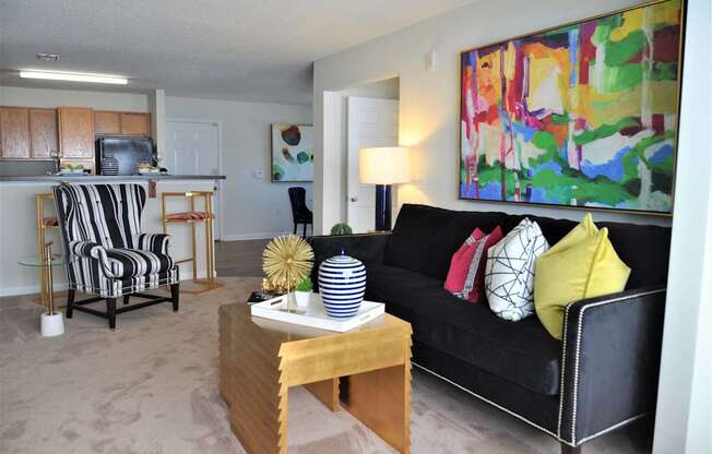 A living room with a black couch and a painting on the wall.