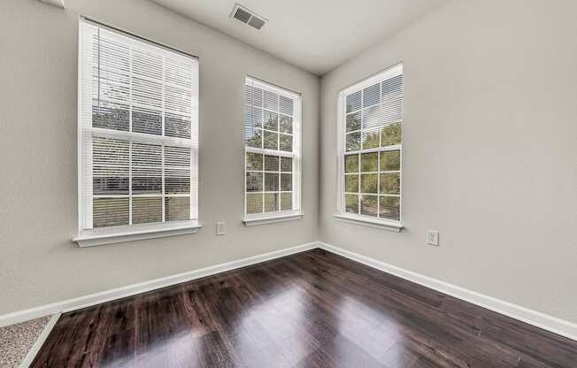 the living room of a new home with wood flooring and three windows