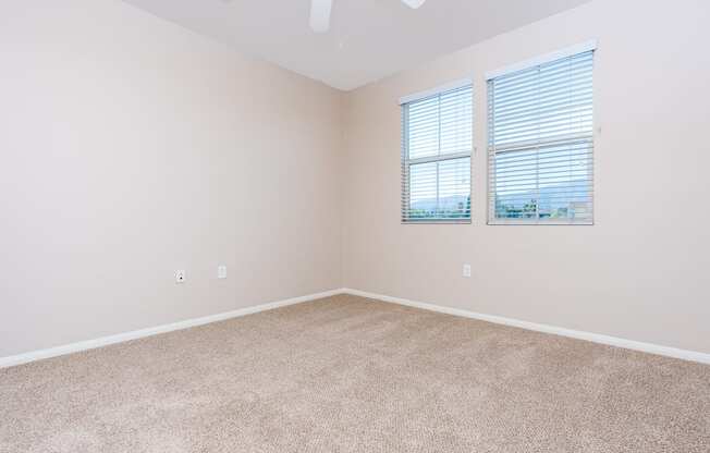 a bedroom with beige carpet and two windows