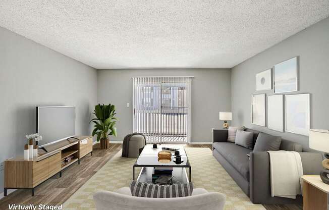 A living room with a grey couch, a wooden entertainment unit, and a large window with a view of a balcony.