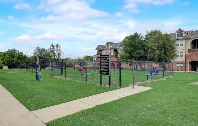 a fenced in dog park with agility equipment and houses in the background
