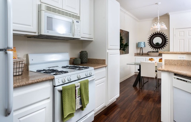 One Bedroom apartments in Rancho Cucamonga CA - Barrington Place - Kitchen with Wood-Style Flooring, Granite Countertops, White Appliances and Cabinets, and Access to Dining Area