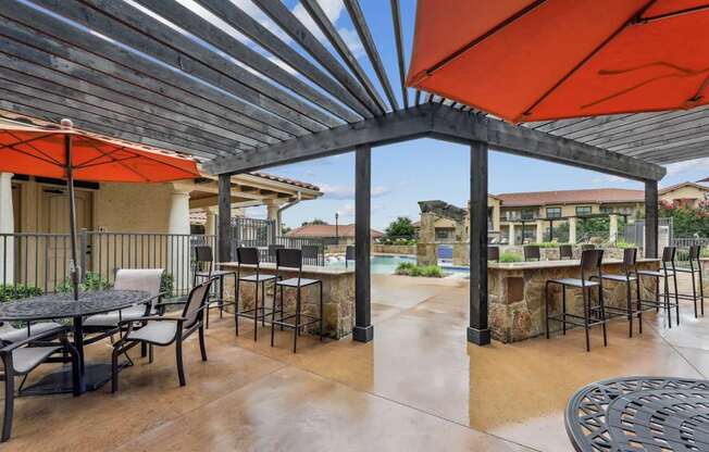 A shaded picnic area with a grilling station, tables, and chairs at Creekside on Parmer Lane Apartments in Austin, TX