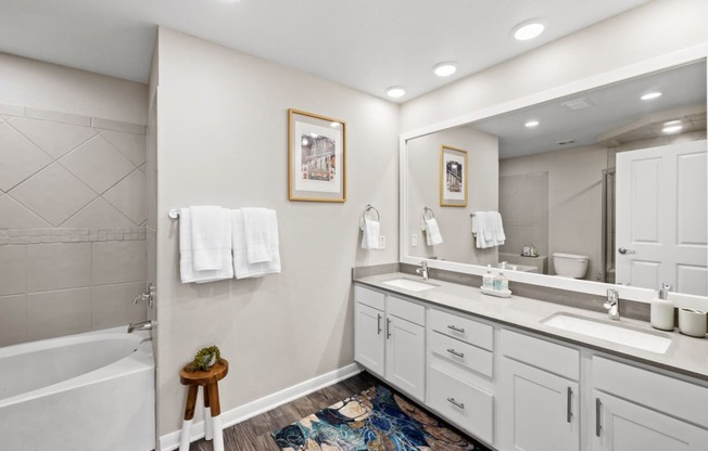 a bathroom with white cabinets and a large mirror and a tub