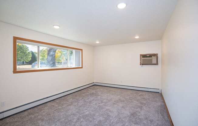 an empty living room with a window and carpet. Fargo, ND Country Club Apartments