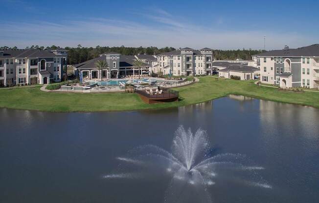 A fountain in the middle of a lake in front of apartment buildings.