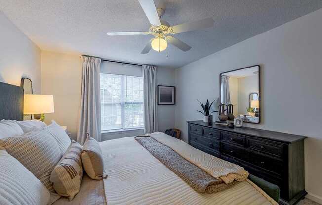 A bedroom with a large bed, a ceiling fan, and a dresser.