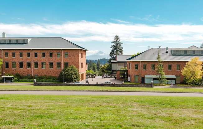 A large red brick building with a black roof is surrounded by a green field.