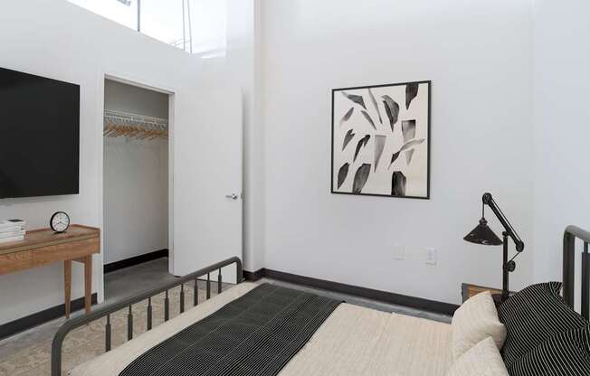 Mill House floor plan bedroom with a bed, a nightstand, a lamp, a wardrobe, and a painting on the wall at Highland Mill Lofts in Charlotte, NC 28205