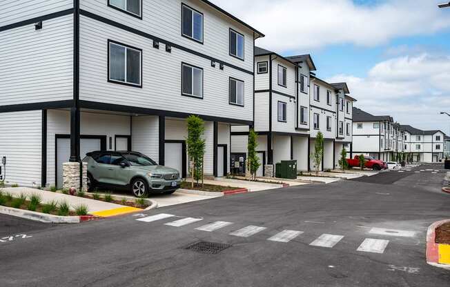 A row of white houses with a green car parked in front of the first one.