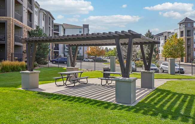 A wooden pergola with a picnic table underneath it is situated in a grassy area.