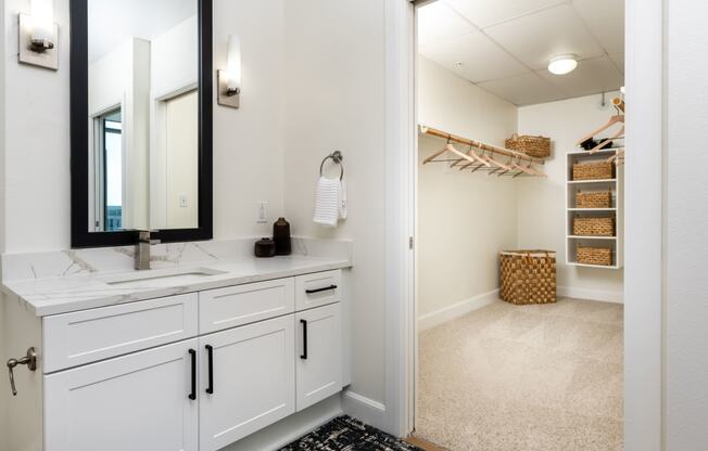 a bathroom with white cabinets and a mirror and a walk in closet