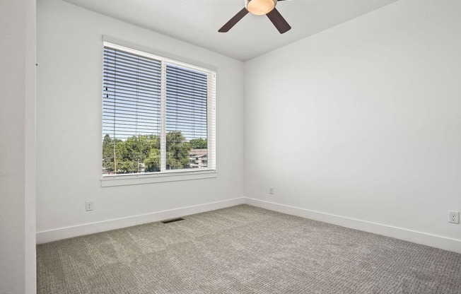 an empty living room with a large window and a ceiling fan  at Aero Luxury Townhomes in Layton, Utah