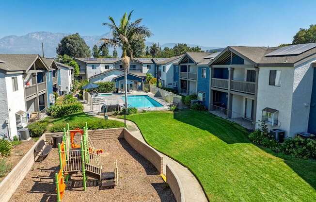 A playground with a slide and swings is surrounded by a grassy area and townhomes.