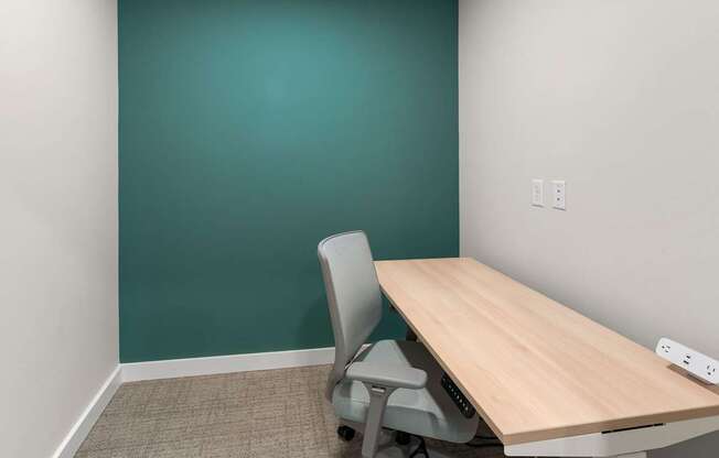A room with a green wall and a wooden table with a grey chair.
