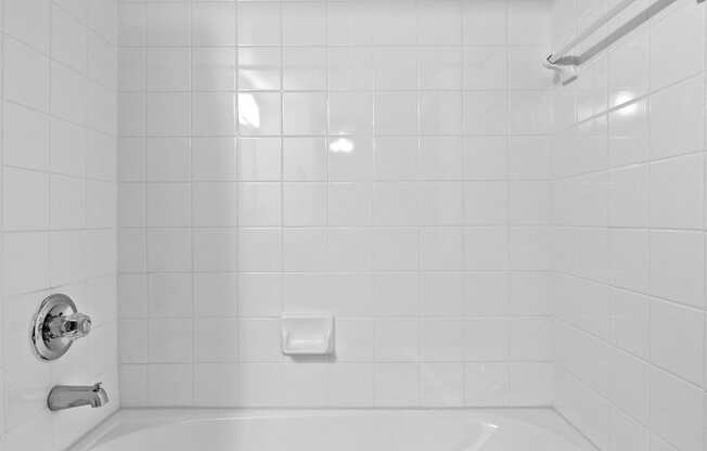 A white bathroom with a white tub and white tiles.