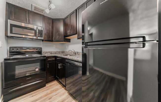 A kitchen with black cabinets and a stainless steel refrigerator.