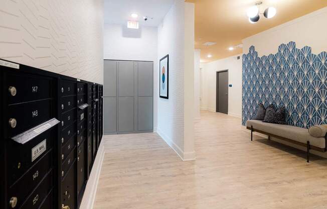 A hallway with a row of black lockers on the left and a bench with a blue and white patterned wall behind it on the right.