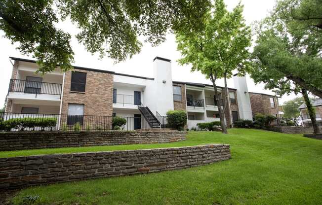 exterior view of apartments with a green lawn and stone retaining wall