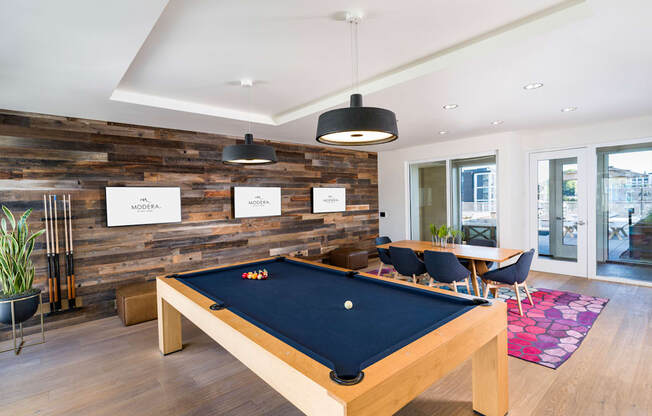 A pool table is in the middle of a room with a wooden wall.