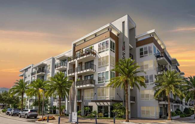 A modern apartment building with balconies and palm trees in front.