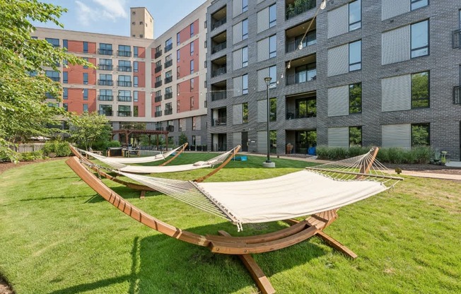 A hammock is set up in a grassy area in front of apartment buildings.