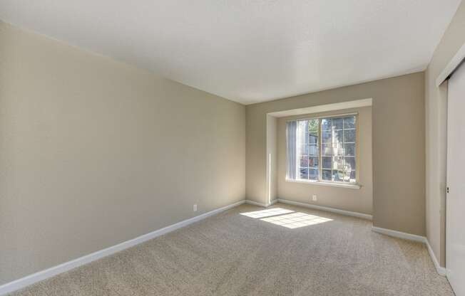 Bedroom with pop- out style window.  Lots of natural sunlight.  Beige walls and light colored carpeting. 