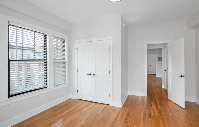 a living room with white walls and wood floors and a door to a hallway