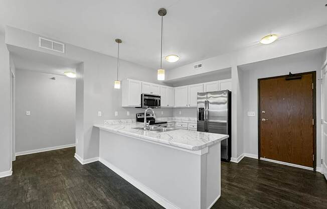 a white kitchen with a large island and a stainless steel refrigerator